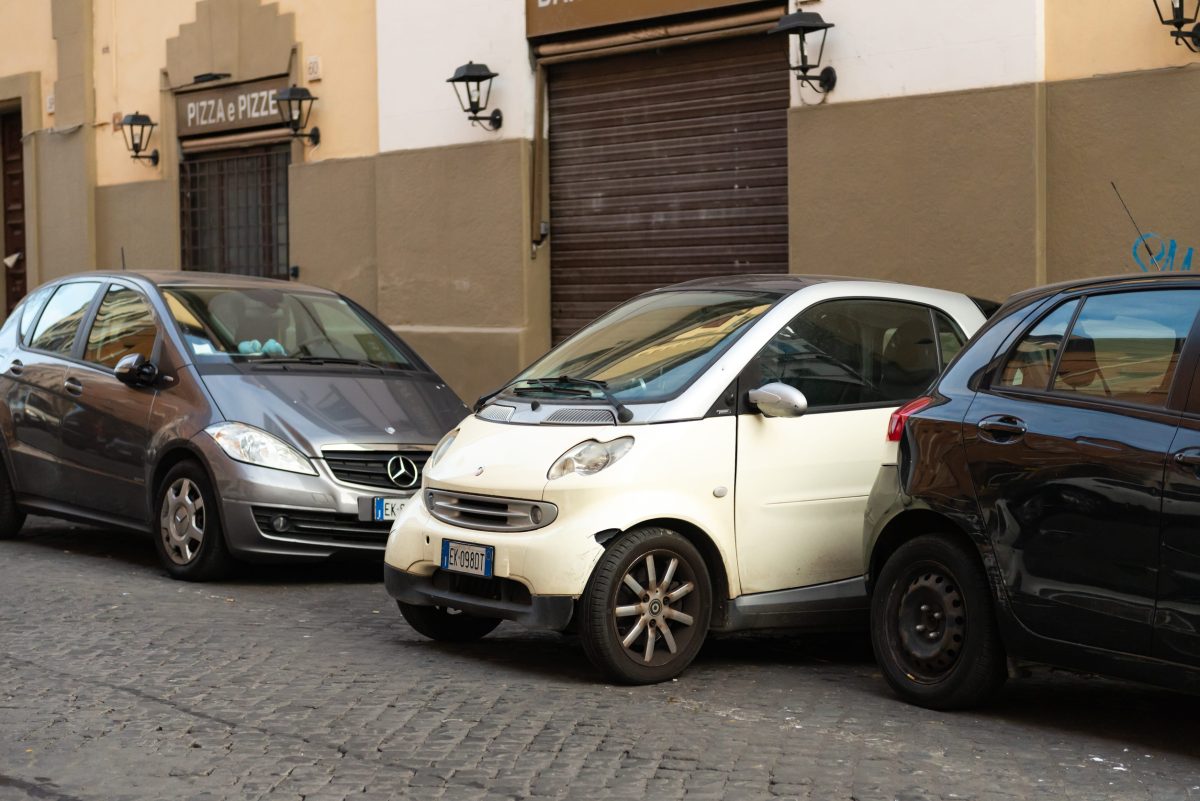 Una piccola auto parcheggiata di traverso su una strada urbana, vicino a un marciapiede