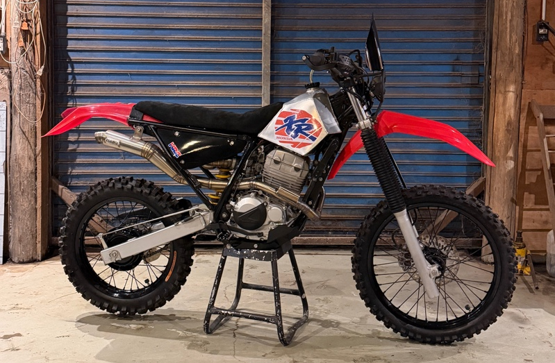 Una Honda XR250 Tornado trasformata in enduro da rally, con serbatoio in alluminio e doppio faro LED, in un garage argentino